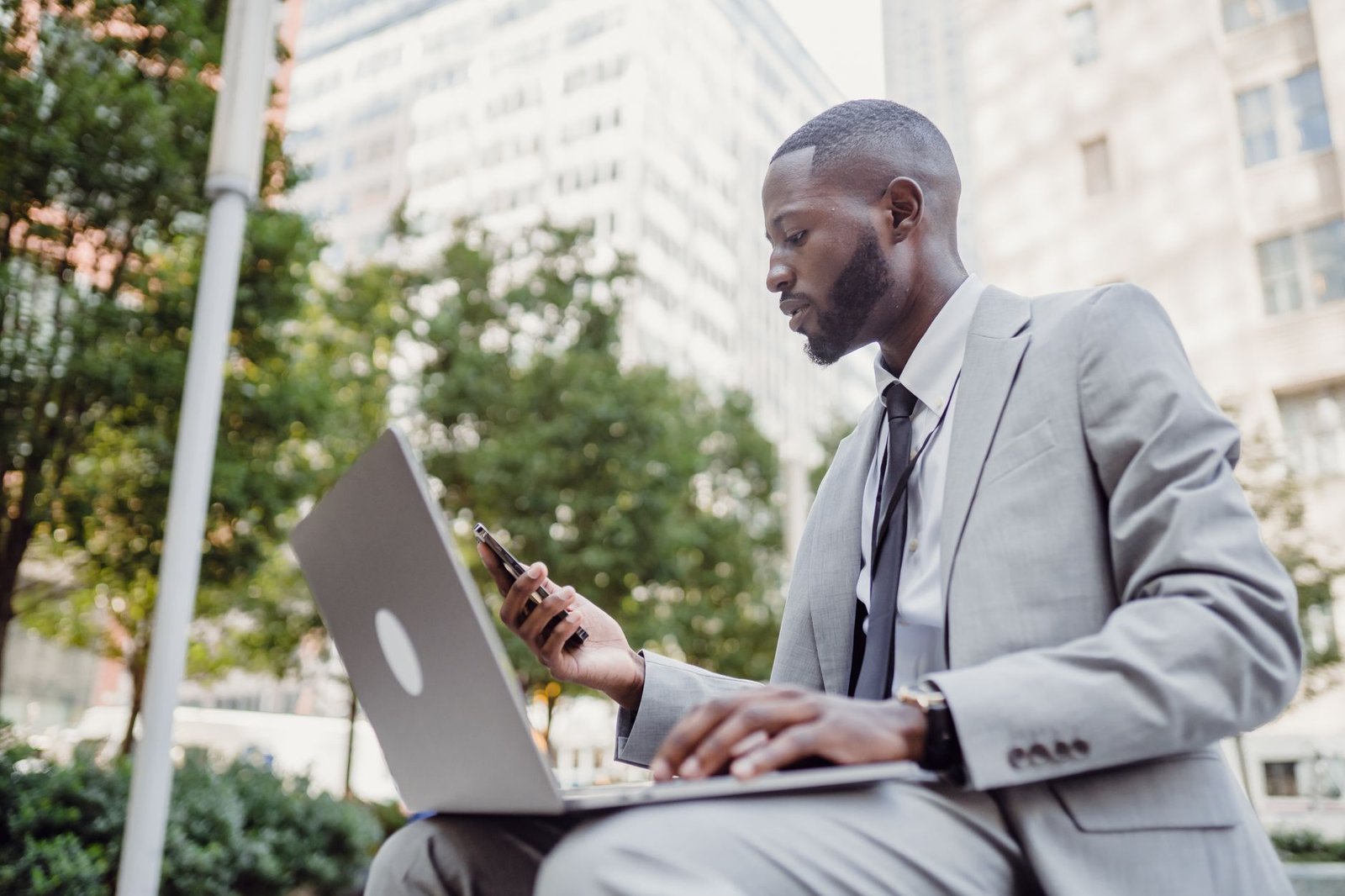 Businessman in a suit using a laptop and smartphone in an urban setting, blending technology with business. — Best Trading In
