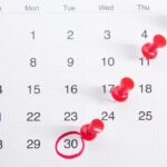 A close-up of a numbered calendar with red thumbtacks marking specific dates, emphasizing an important renewal date.