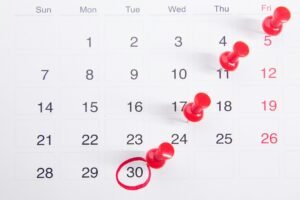 A close-up of a numbered calendar with red thumbtacks marking specific dates, emphasizing an important renewal date.